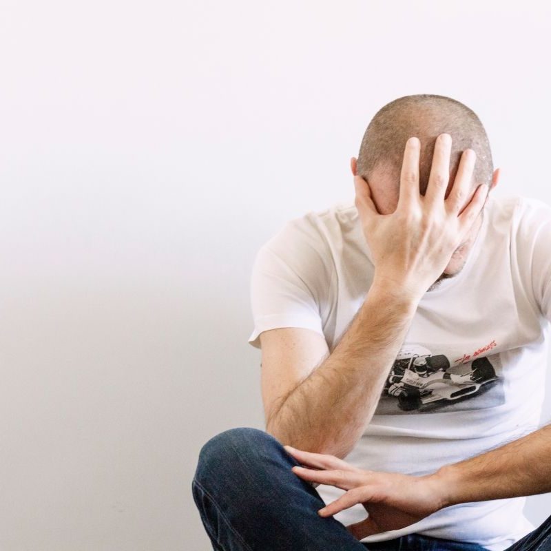 man-looking-depressed-with-a-hand-on-head-sitting